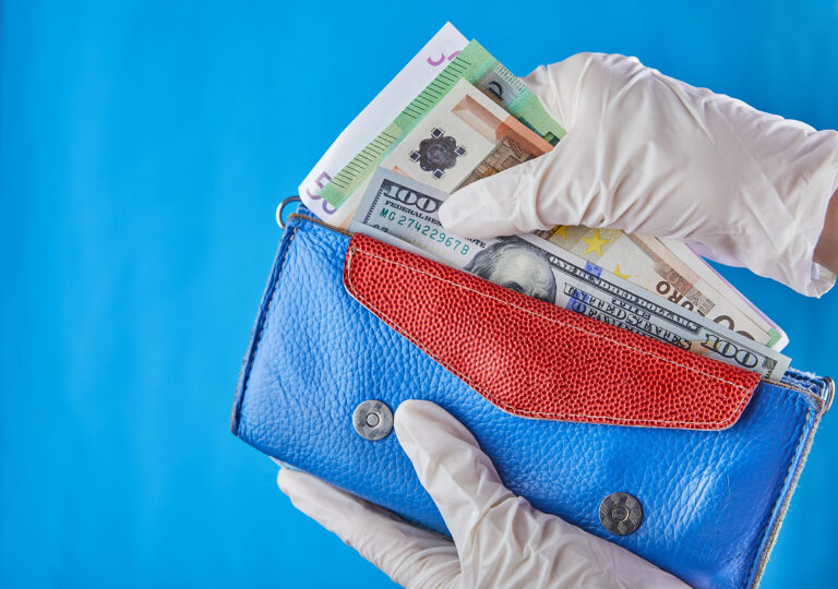 A woman taking money out of her wallet wearing rubber gloves to prevent the spread of bacterias or viruses or shopping during coronavirus pandemic